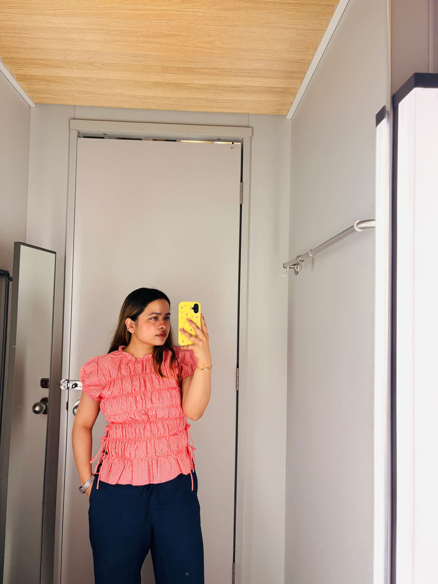 Soumya Singh in a coral gingham top and navy trousers against a pale grey wall